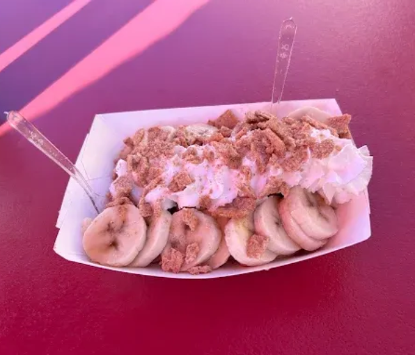 Dessert bowl with banana slices, whipped cream, and crumbled topping on a red table
