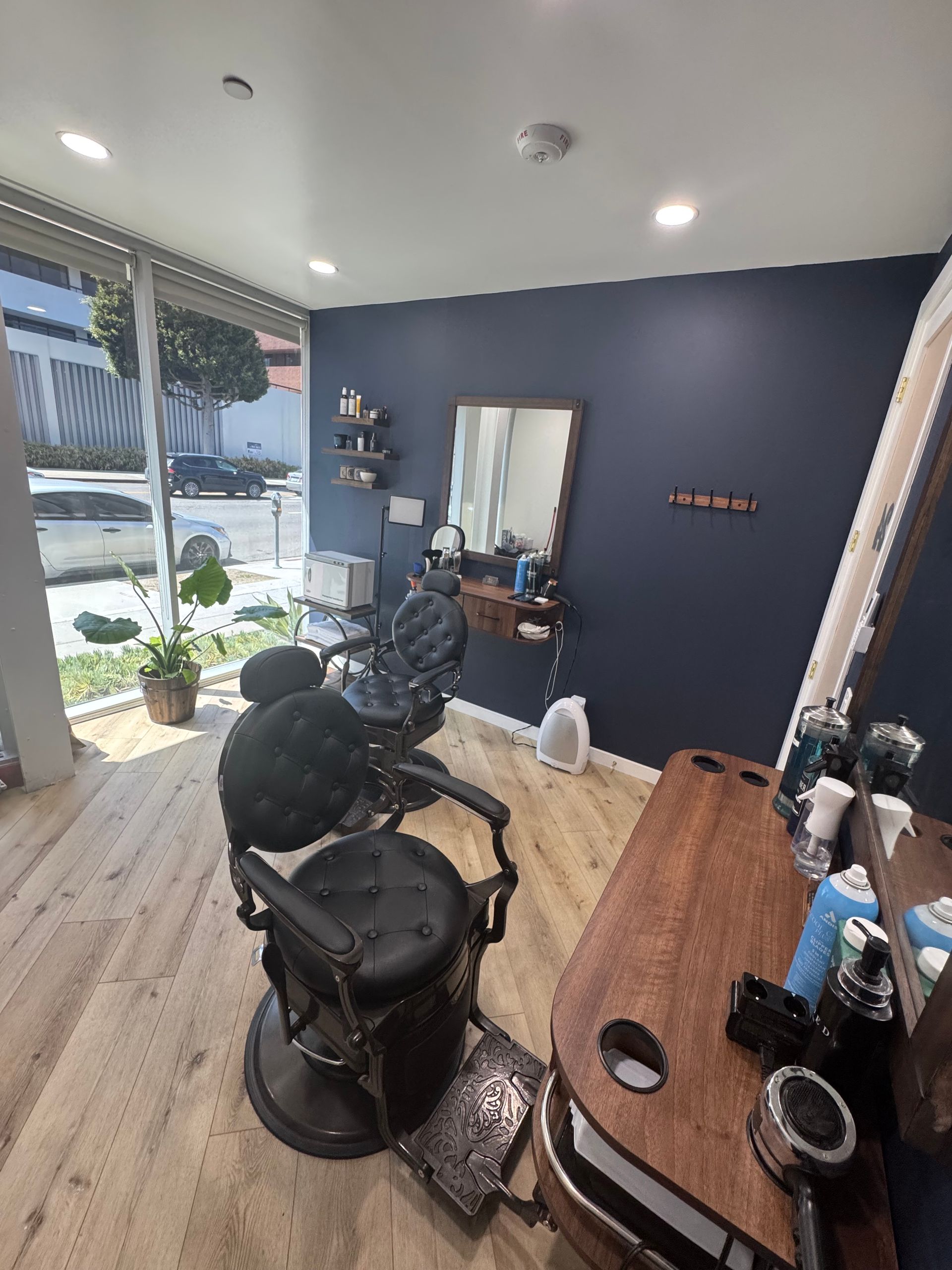 Barbershop interior with two black chairs, wall mirror, and sunlight through the glass door.