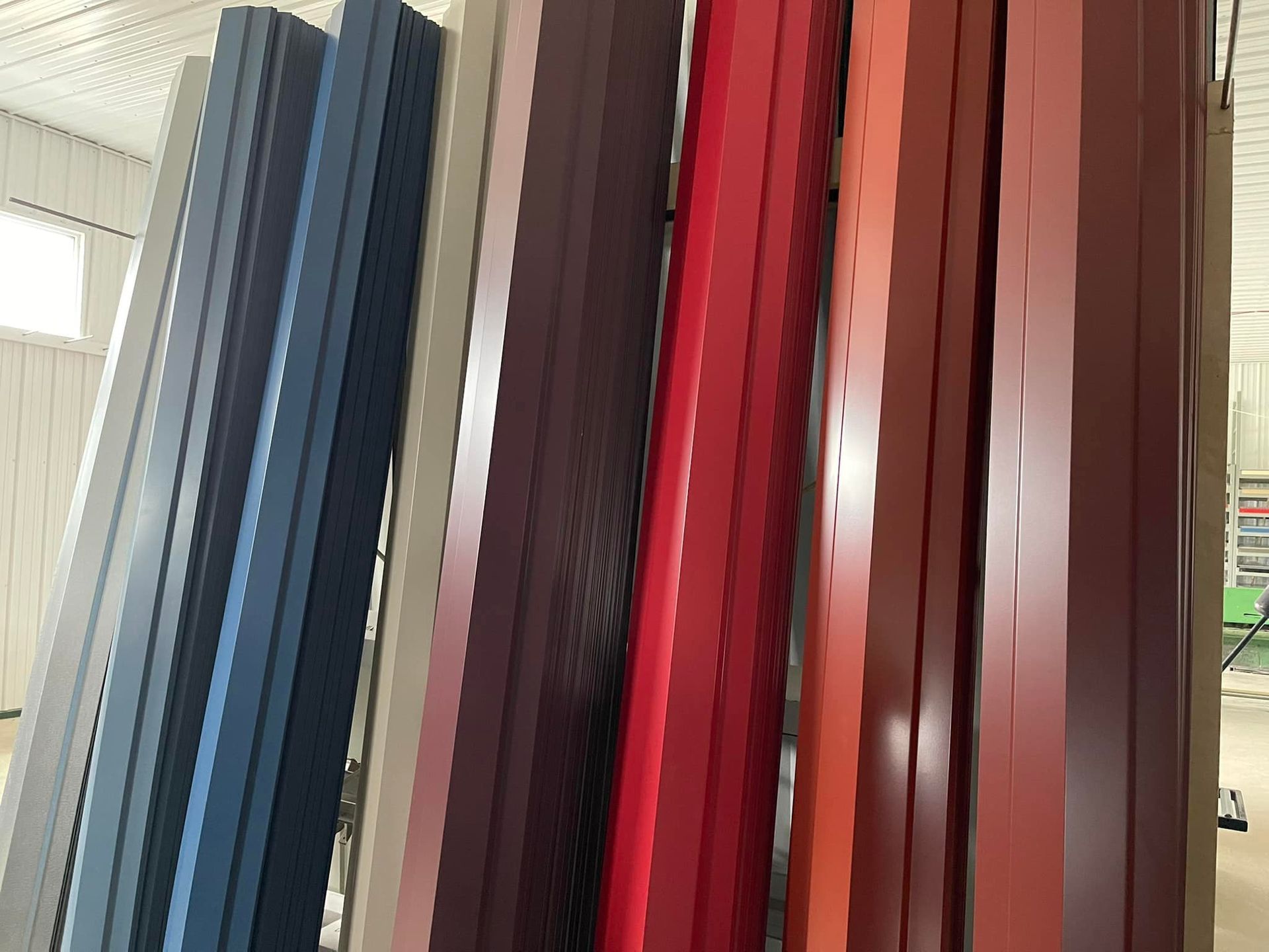 Colored metal panels leaning against a wall, showcasing a range of hues from blue to red and brown.