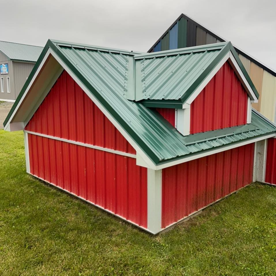 Red and white barn-style shed with a green metal roof. Sitting on green grass.