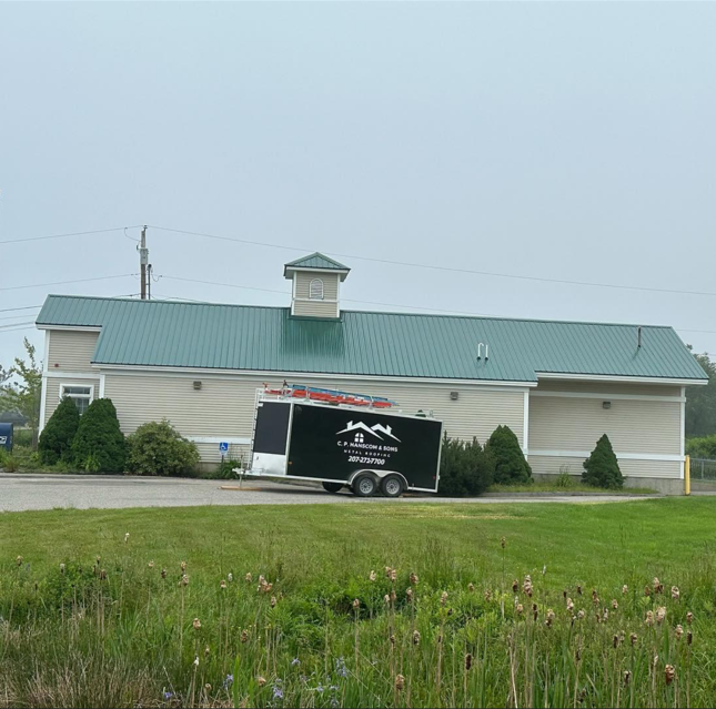 A building with a green roof and a black trailer parked in front on a cloudy day.