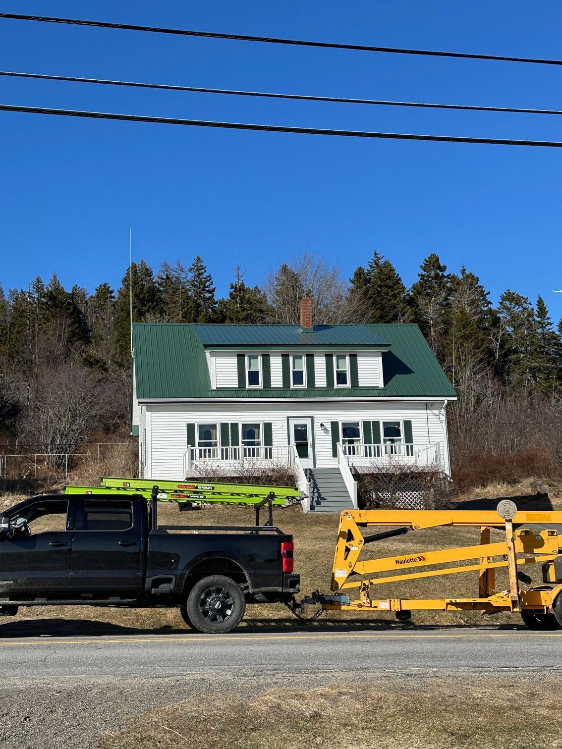 White house with green roof, a truck pulling equipment on a sunny day.