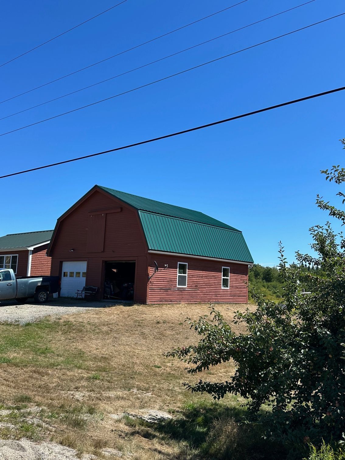 Red barn with green roof, white garage door, and small windows against a bright blue sky.