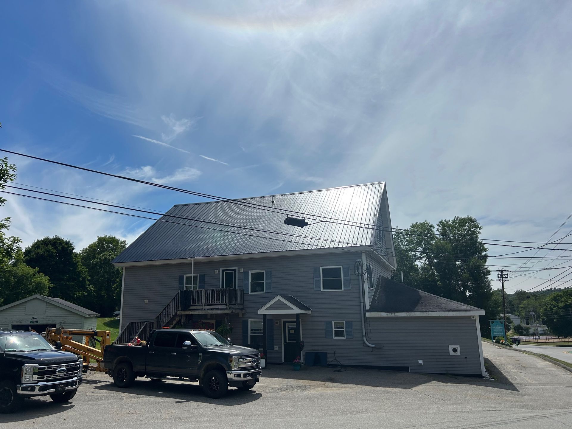 Two-story gray building with a metal roof. A black truck is parked in front of it. A solar halo is in the sky.