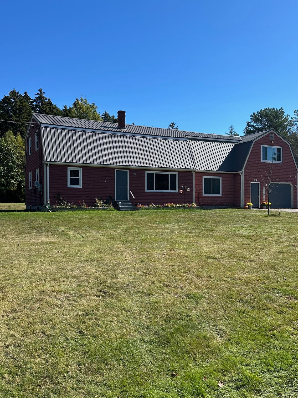 Red house with a dark roof and green yard under a blue sky.
