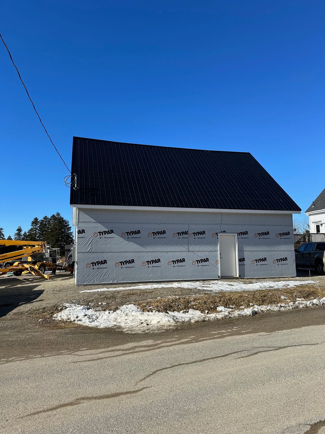 Building under construction, gray siding and black roof, blue sky background.