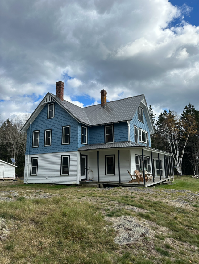 Two-story blue and white house with porch, under cloudy sky.