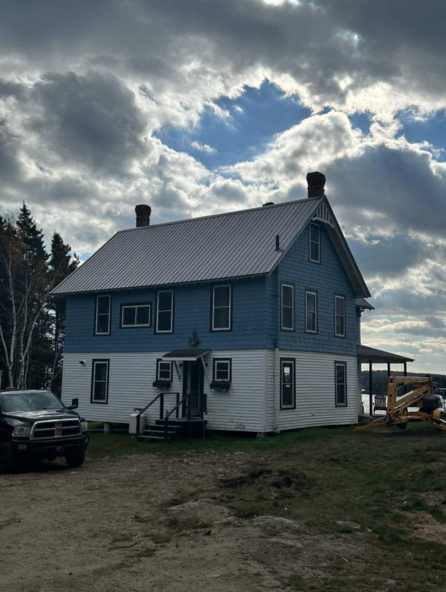 Blue and white two-story house under a cloudy sky, with a truck parked in front.