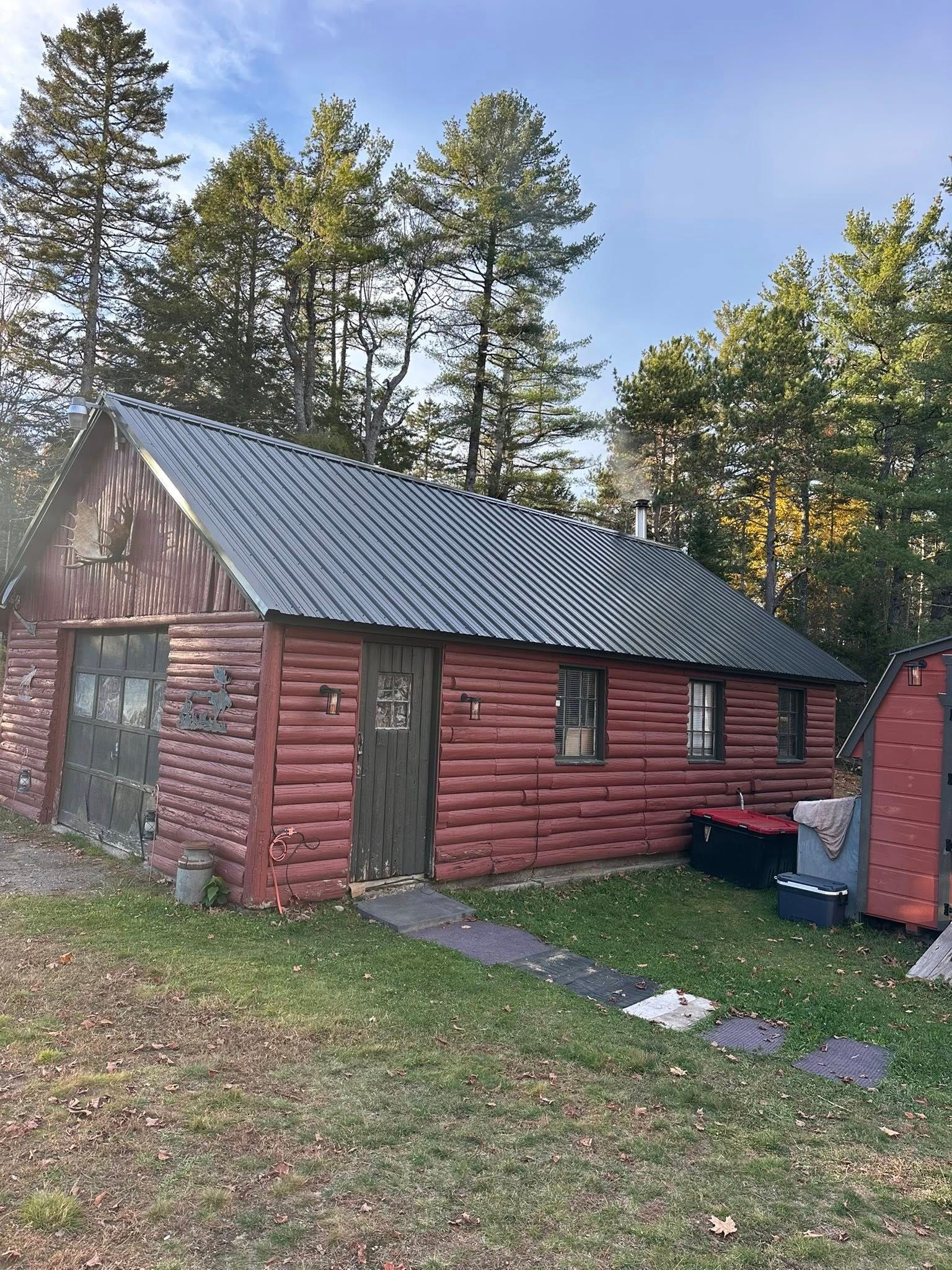 Red log cabin with garage door, small door, metal roof, and surrounding trees.