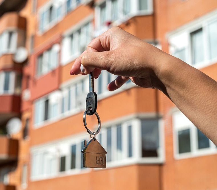 woman real estate agent hands over the keys to a new house against the background of a new building. the concept of selling or transferring an apartment