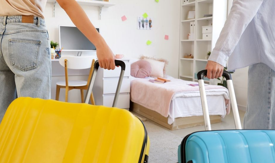 Female students with suitcases in a room on moving day, back view