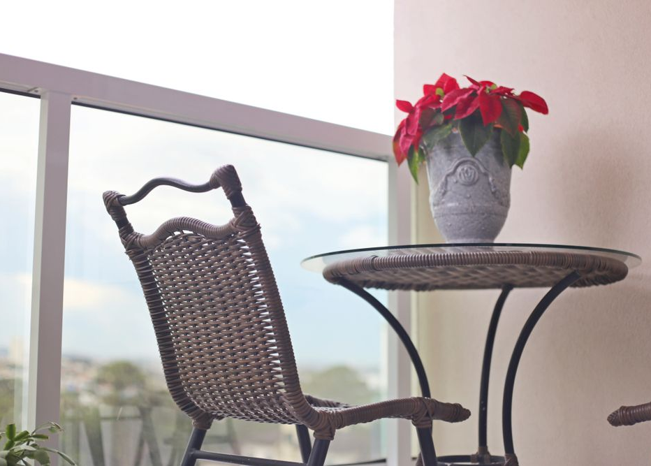 Chair and small metal table on the balcony of the apartment. On a table a vase with red flowers decorating the room.