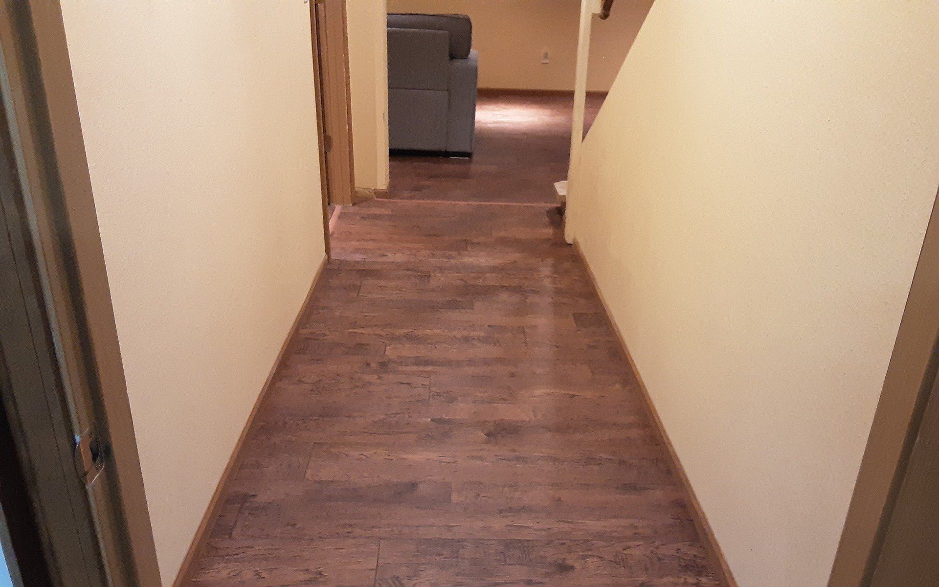 Narrow hallway with beige walls, wood floor, and a chair at the far end.