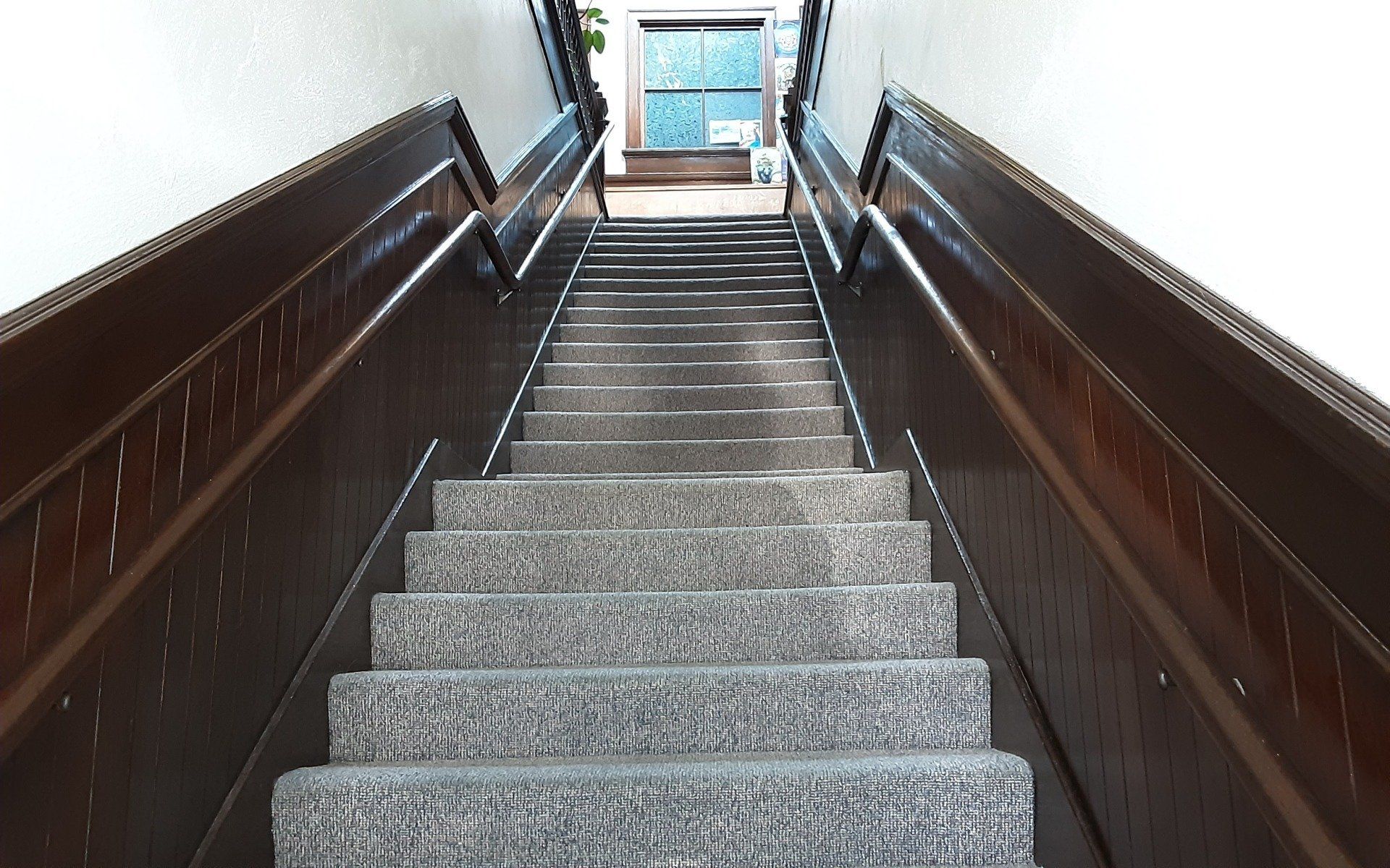 Staircase with dark wooden railings and carpeted steps leading to a bright doorway above