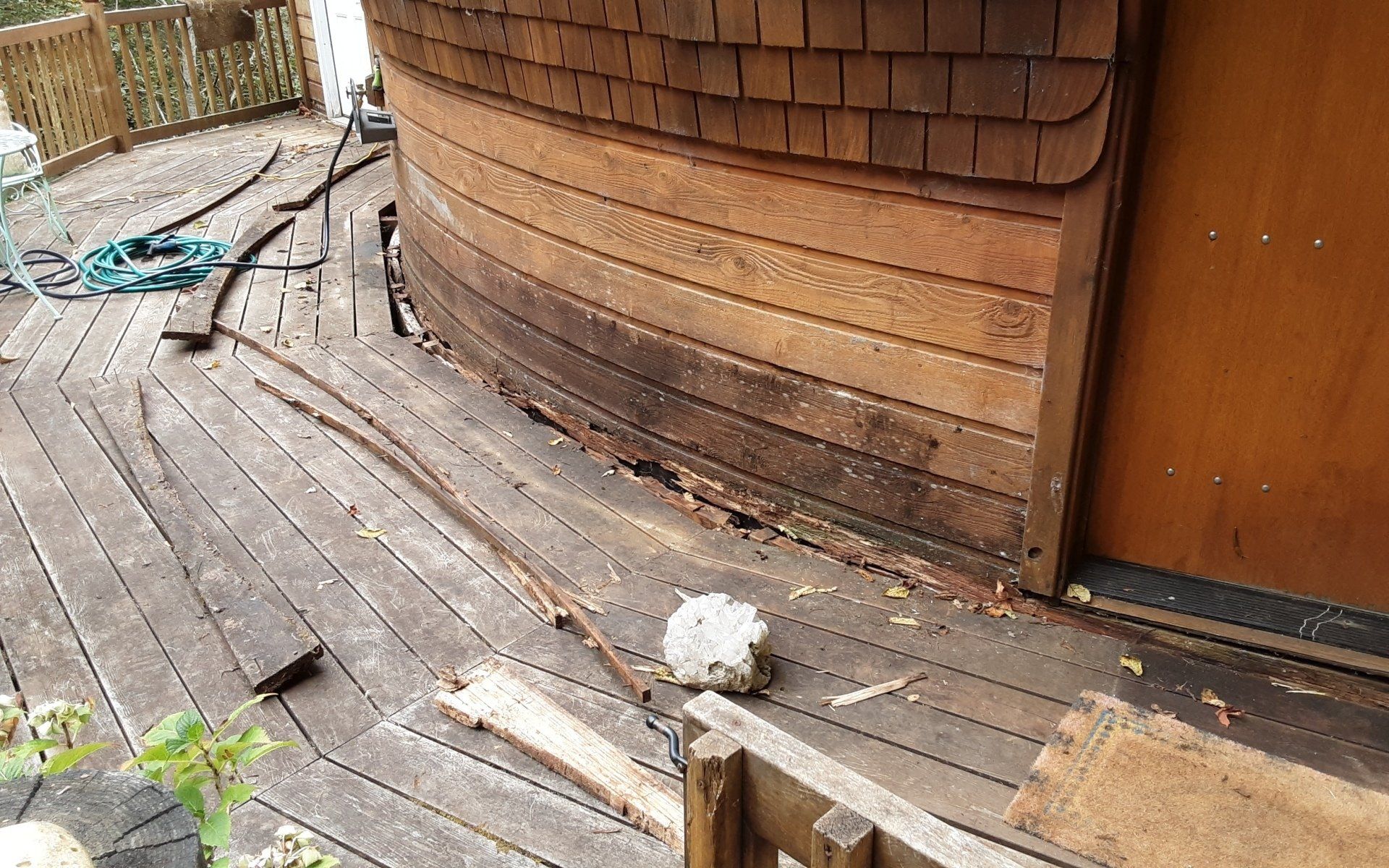 Weathered wooden deck beside a curved brown building, with a small white fluffy dog near scattered debris.