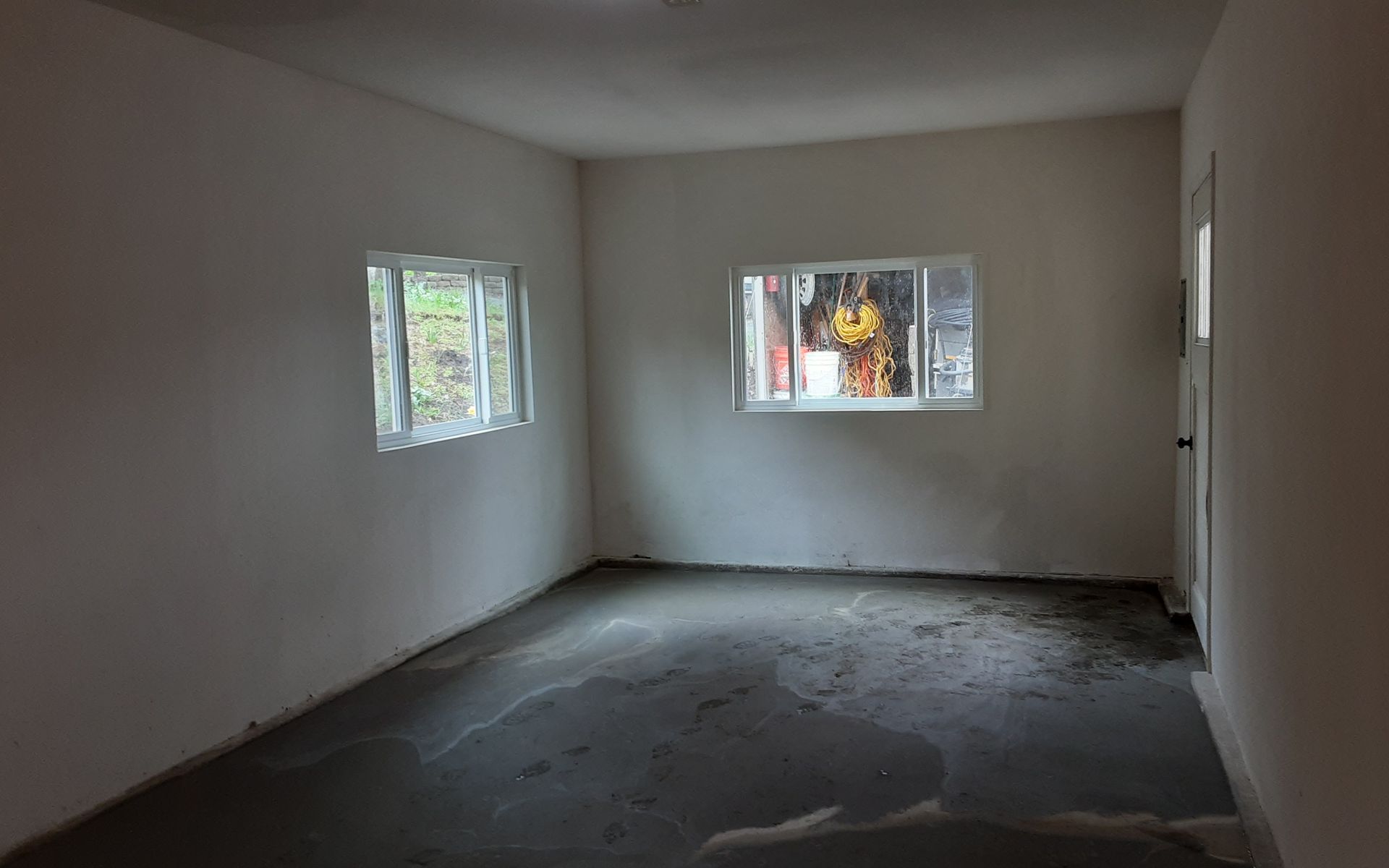 Empty unfurnished room with white walls, two small windows, and a bare concrete floor.