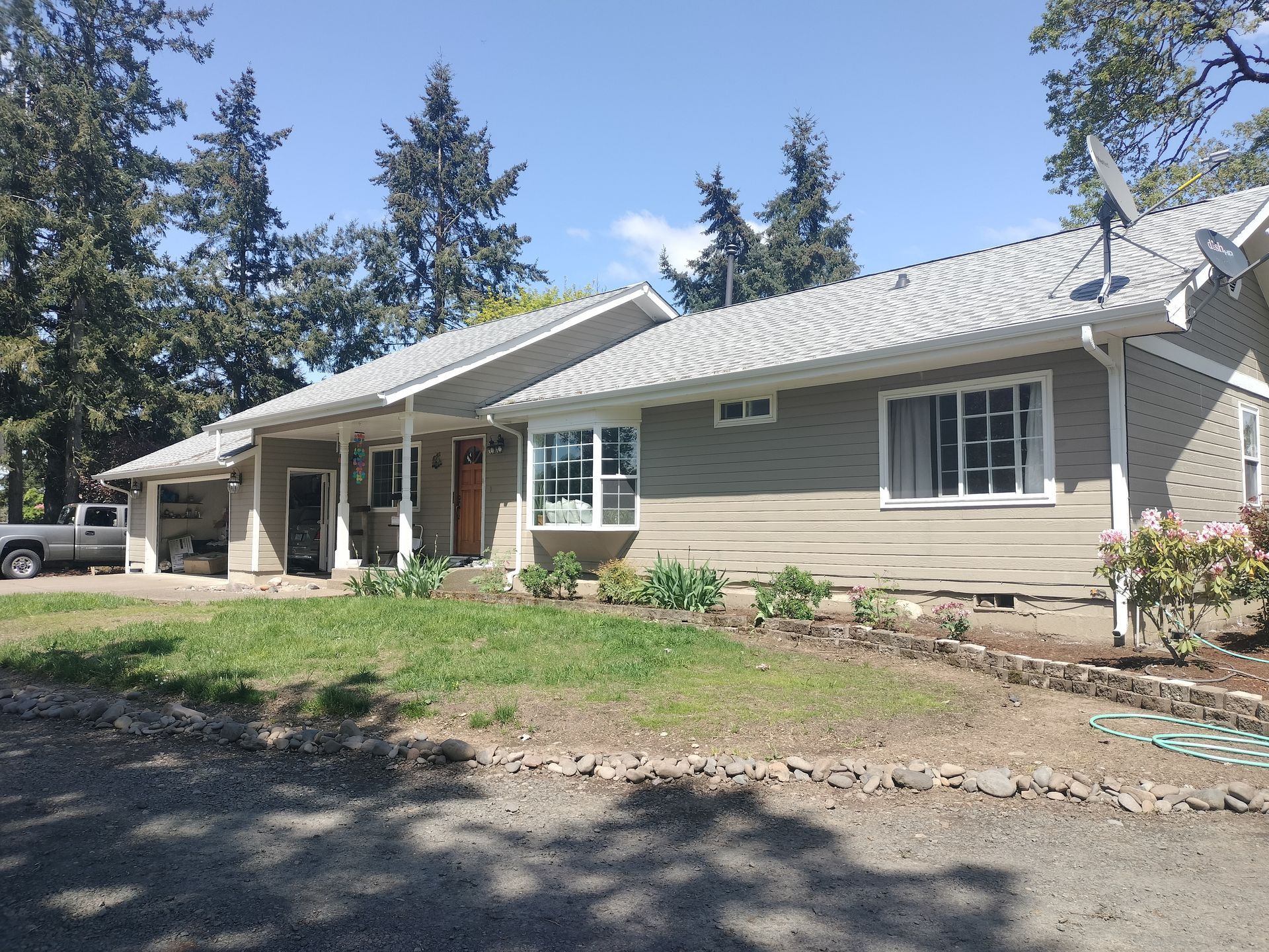 Single-story beige house with white trim and a metal roof, surrounded by trees and a yard.