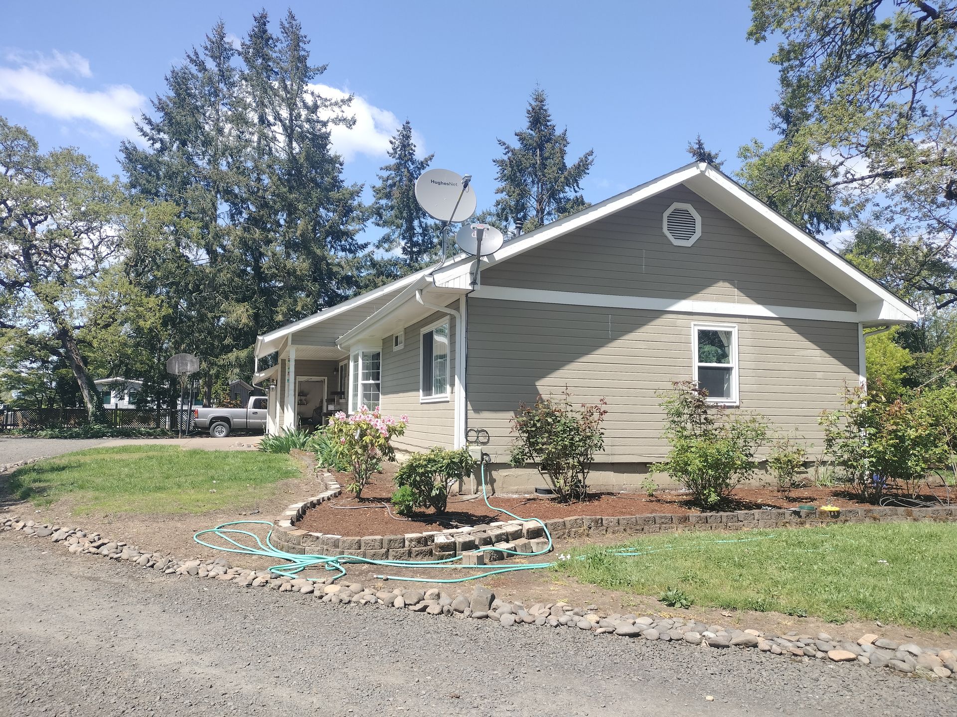 Single-story beige house with white trim, satellite dish, and a landscaped yard with trees.