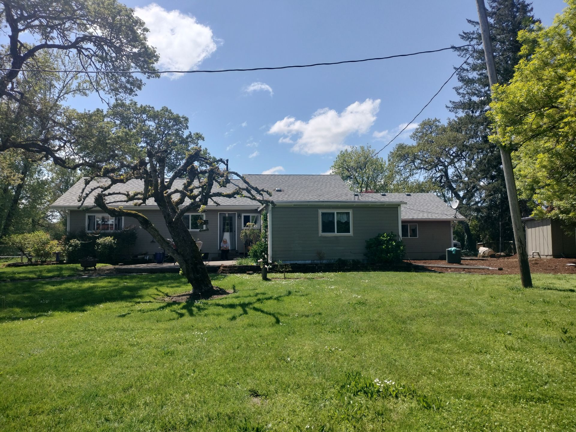 Single-story gray house with a large green lawn and trees under a blue sky