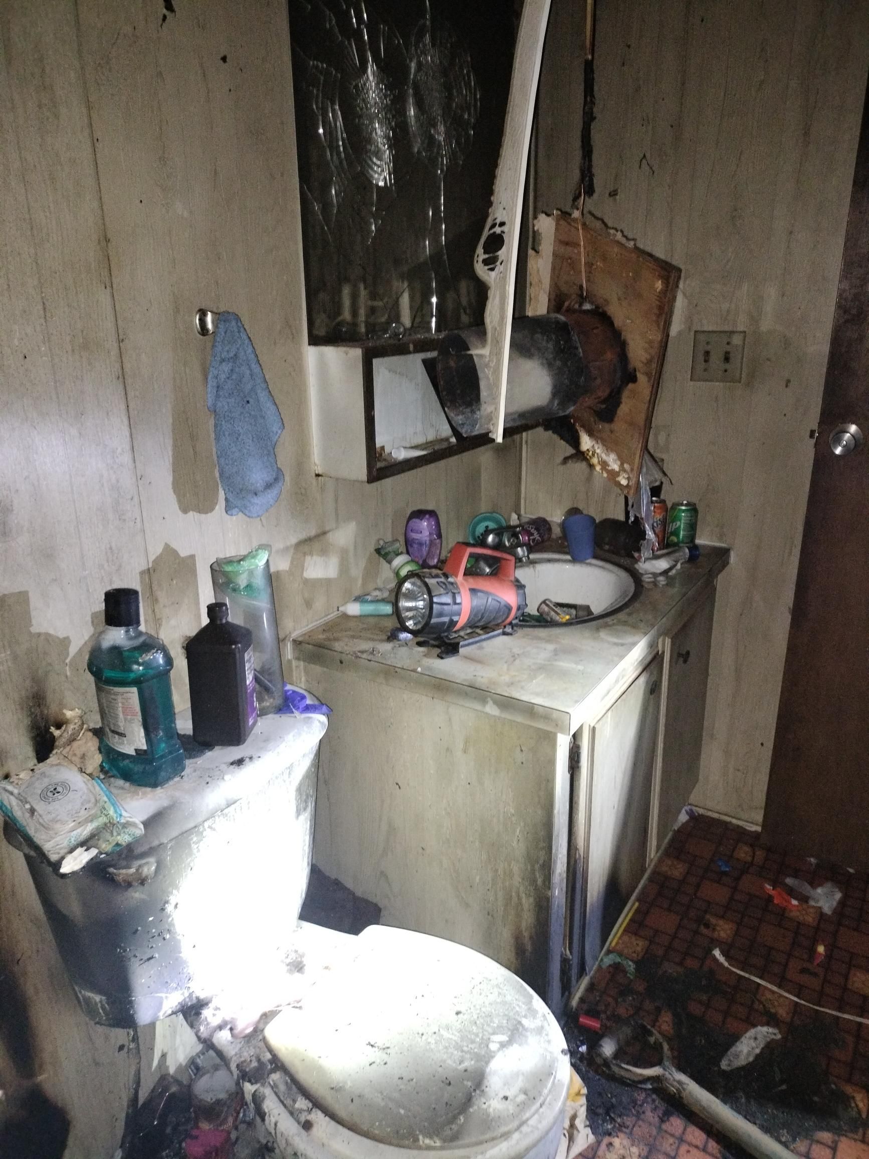 Damaged kitchen with a broken sink, cluttered counter, and fire damage on the wall and ceiling