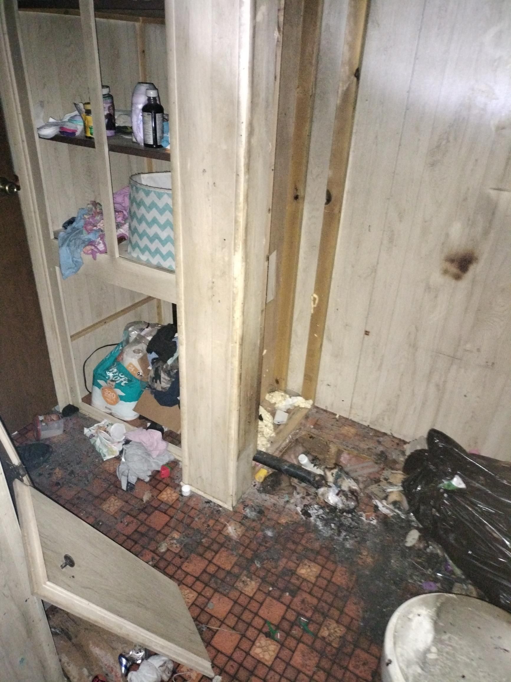Damaged bathroom cabinet with broken shelves, scattered toiletries, and debris on the floor.