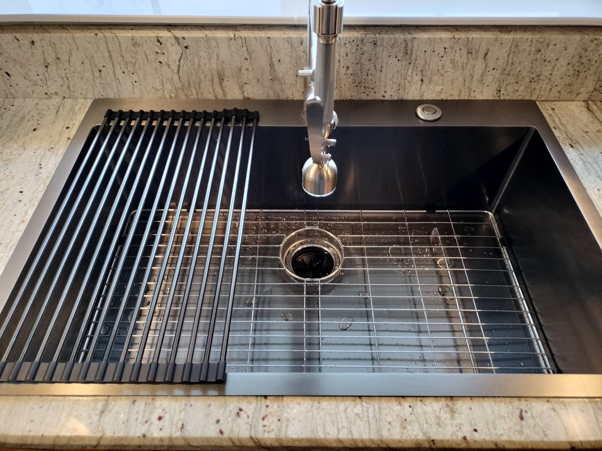 Stainless steel kitchen sink with faucet, black basin, and drying rack in a beige countertop