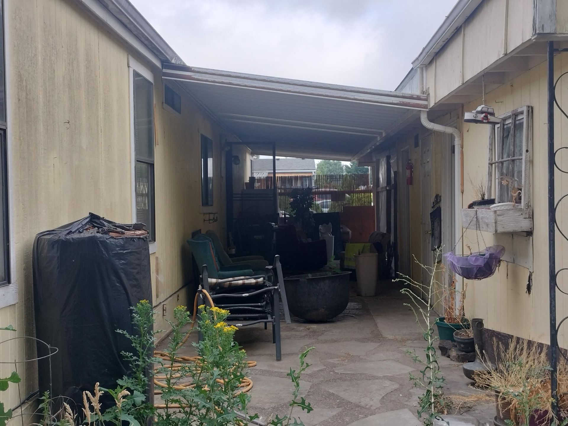 Narrow courtyard between two buildings with stacked chairs, potted plants, and a covered walkway