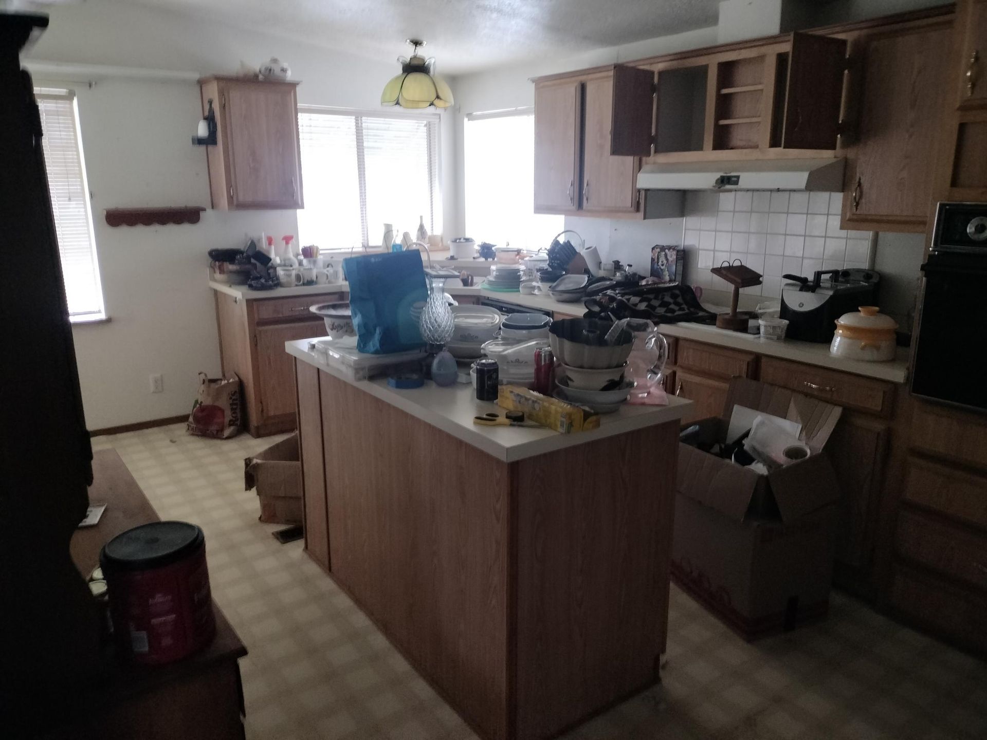 Cluttered kitchen with wooden cabinets, central island, and dishes on countertops near a bright window.