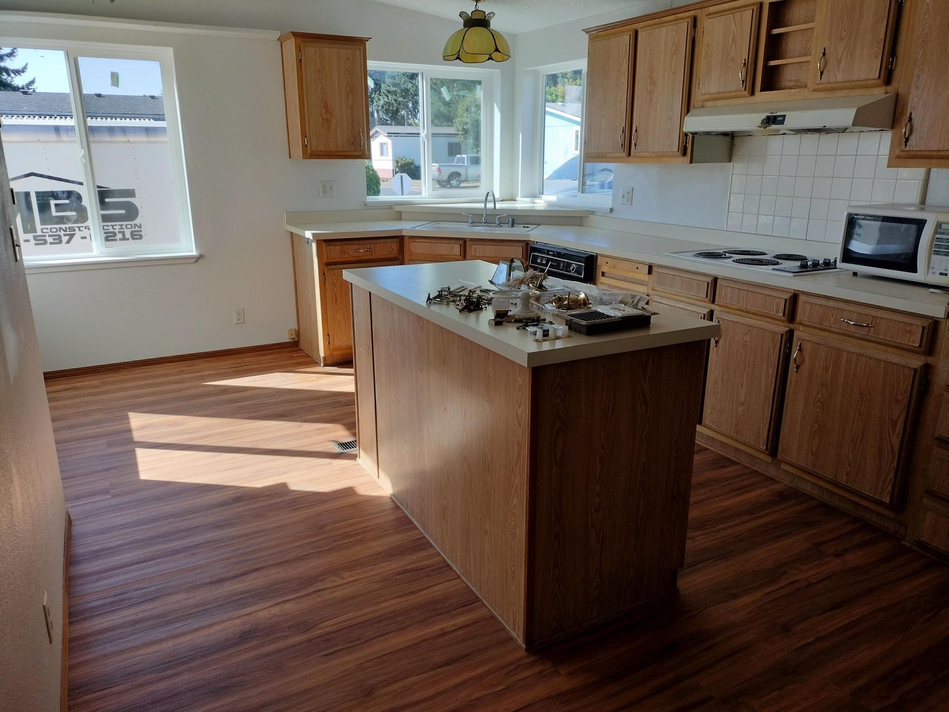 Bright kitchen with wooden cabinets, island, hardwood floor, and sunlight from windows