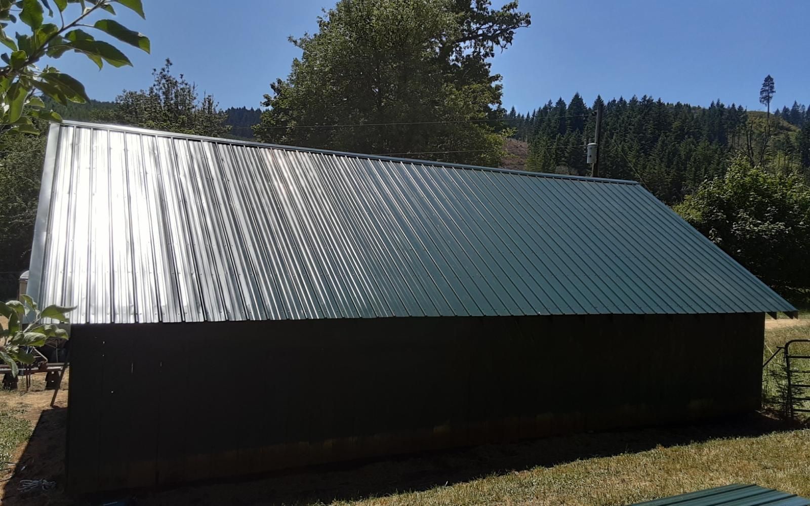 Black building with a shiny silver metal roof in a wooded rural setting