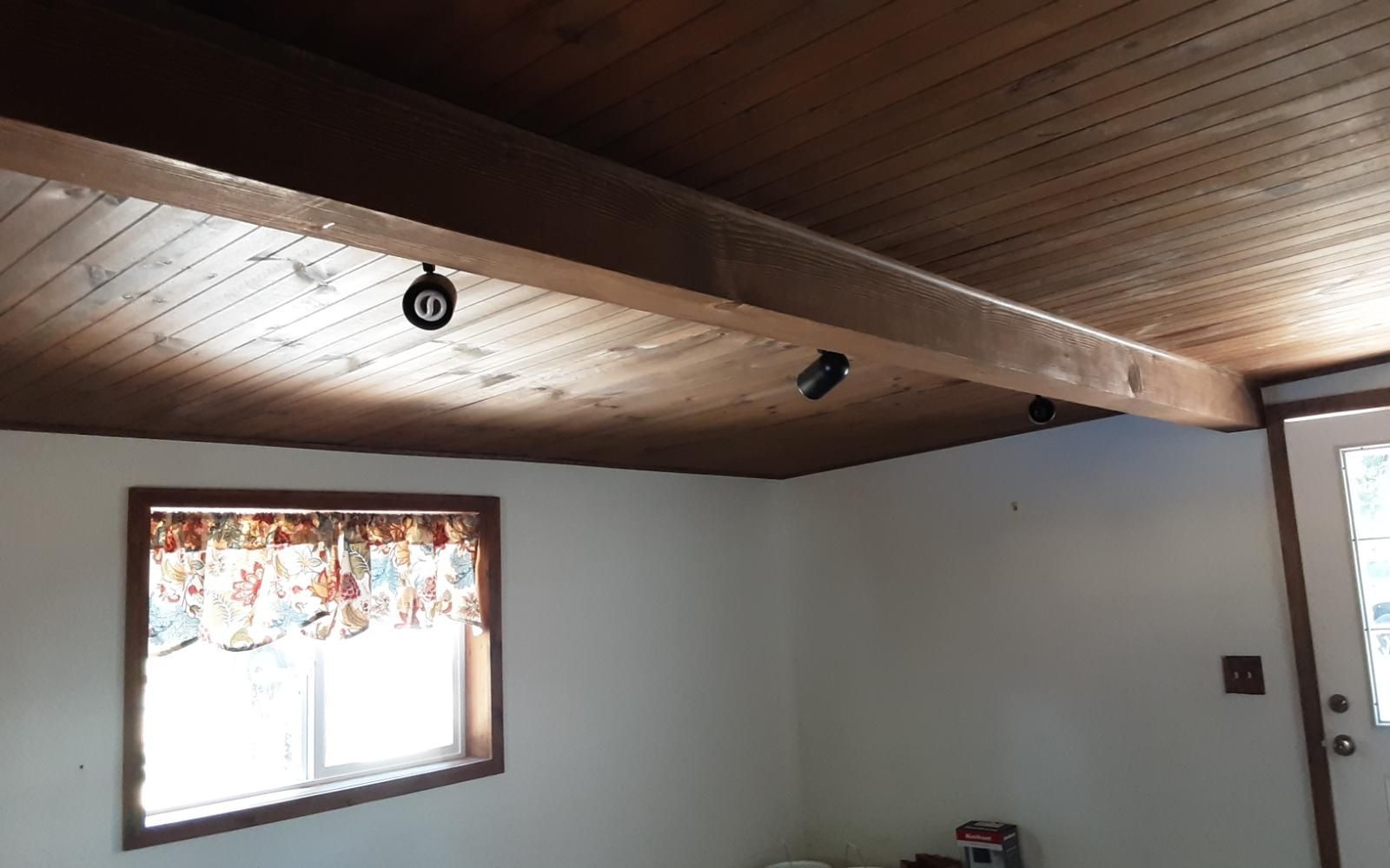 Small room with wood-paneled ceiling, white walls, and two windows letting in daylight.