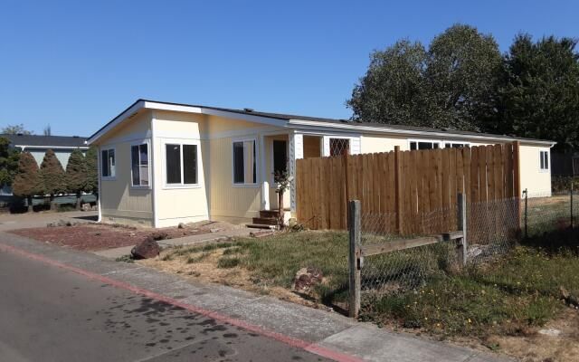 Single-story cream house with a wooden fence beside a paved street under a clear sky