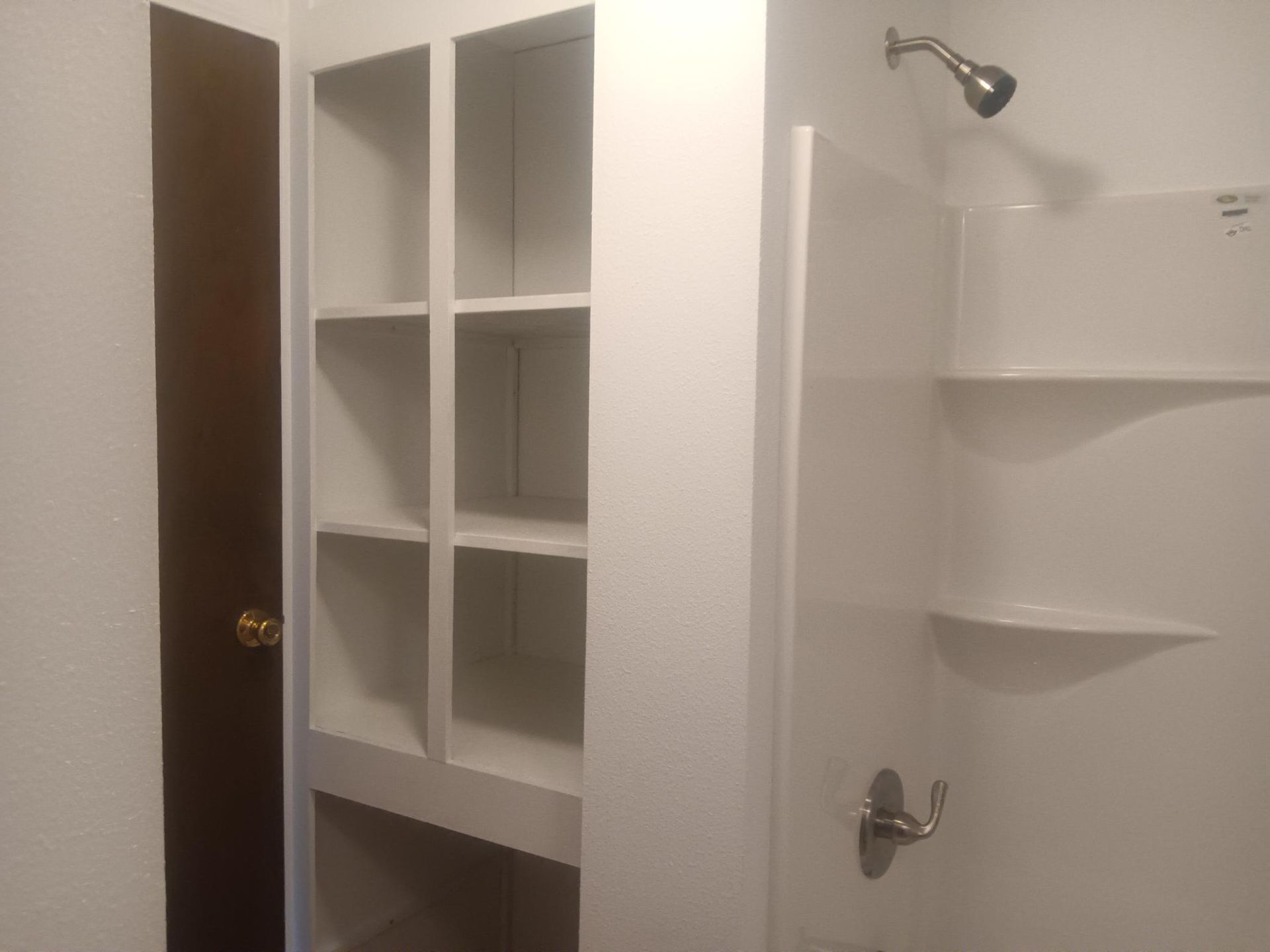 Bathroom with white built-in shelves, a wall sconce, and a shower area with fixtures.