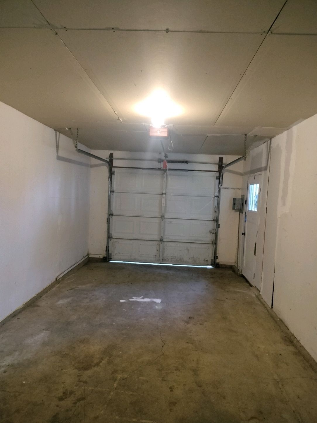 Empty garage interior with closed white overhead door, concrete floor, and ceiling light