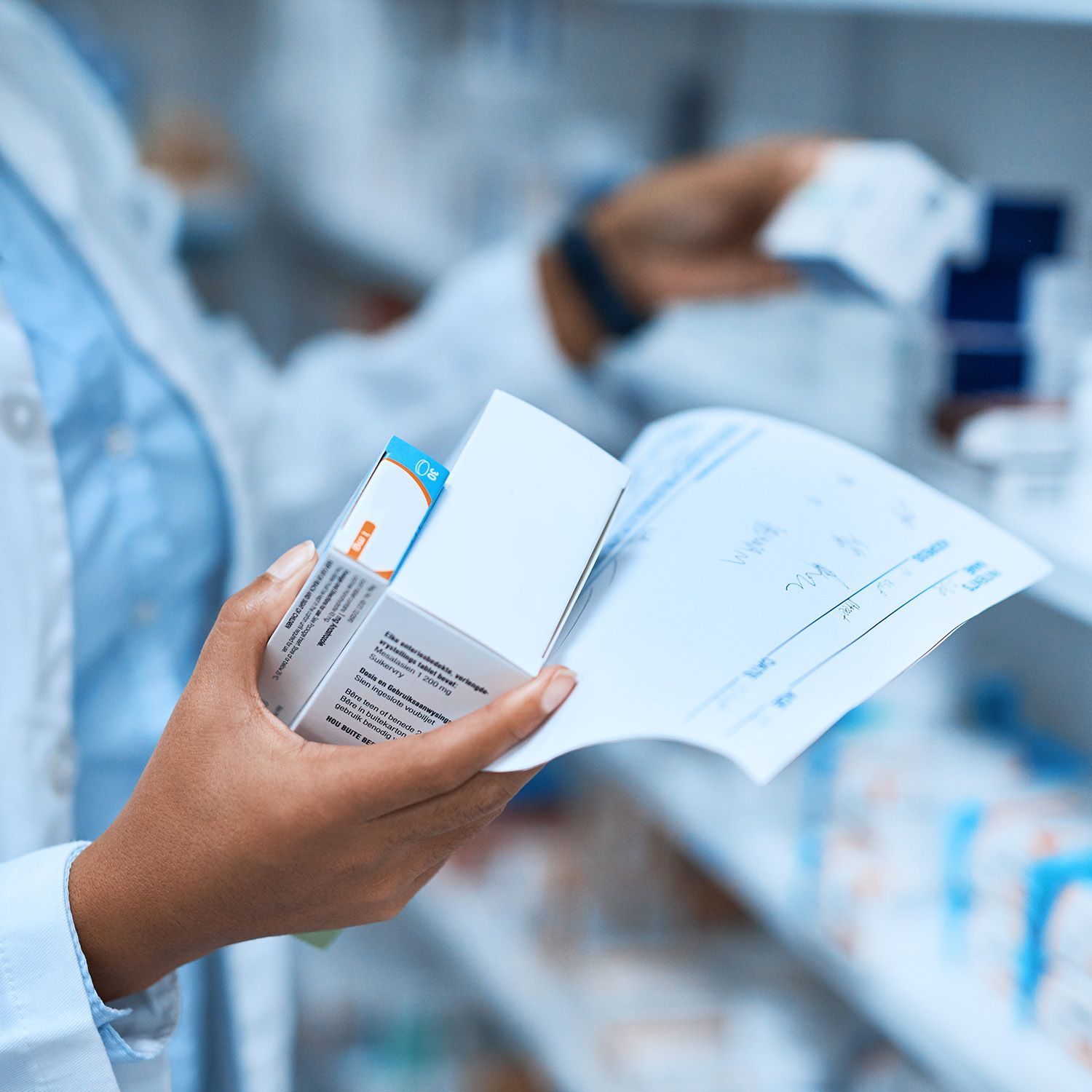 A pharmacist is holding a box of pills and reading a prescription.