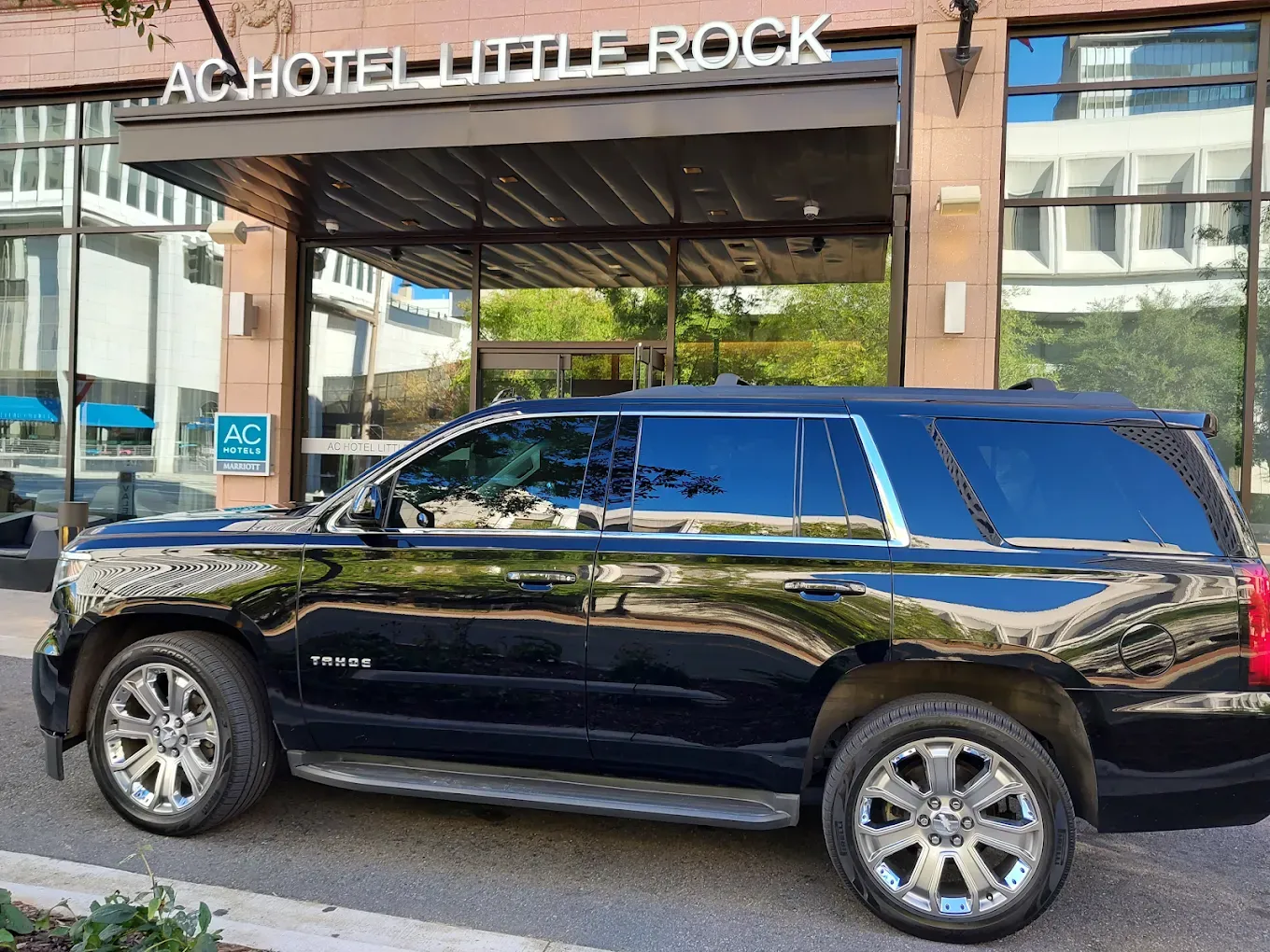 Black SUV parked in front of AC Hotel Little Rock. Shiny exterior, chrome wheels, building entrance.