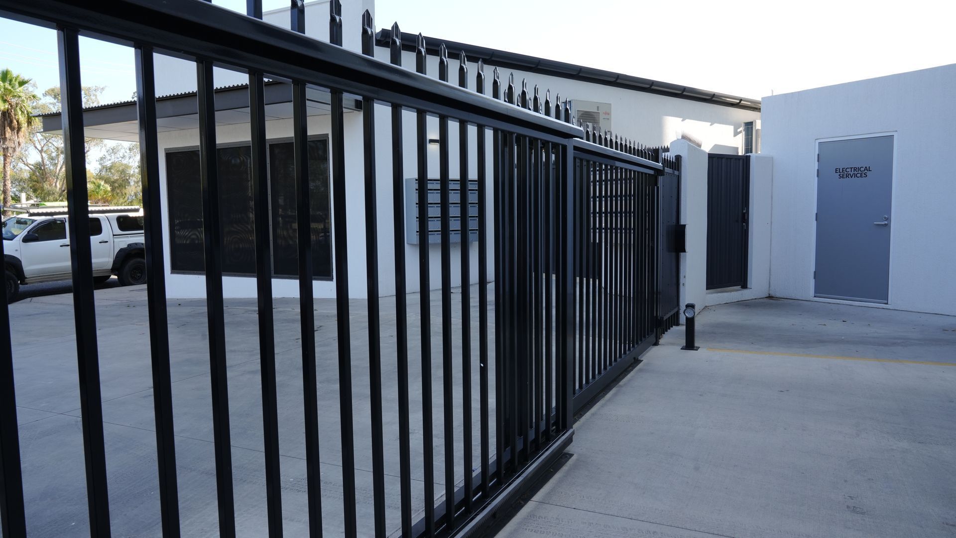 Black metal fence beside a concrete walkway outside a white building with a gray door