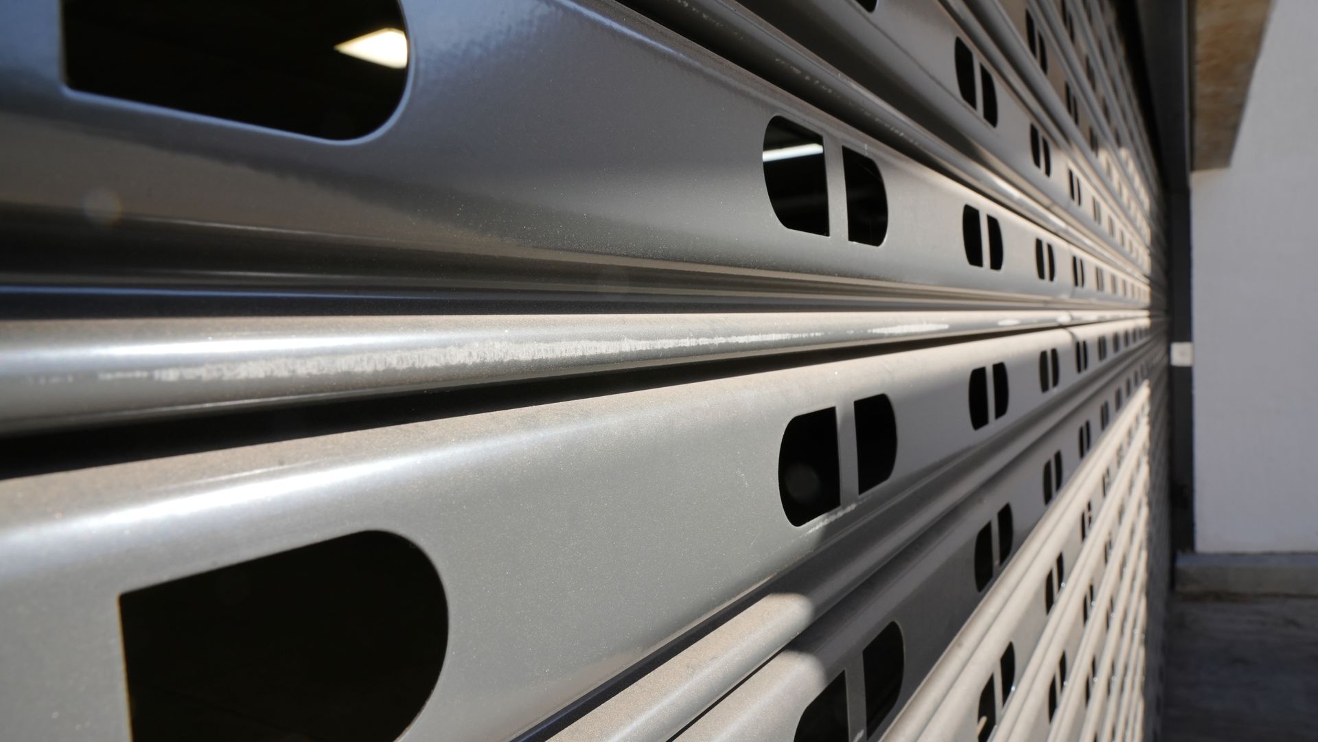 Close-up of a gray metal roller shutter with rows of oval ventilation openings in a corridor