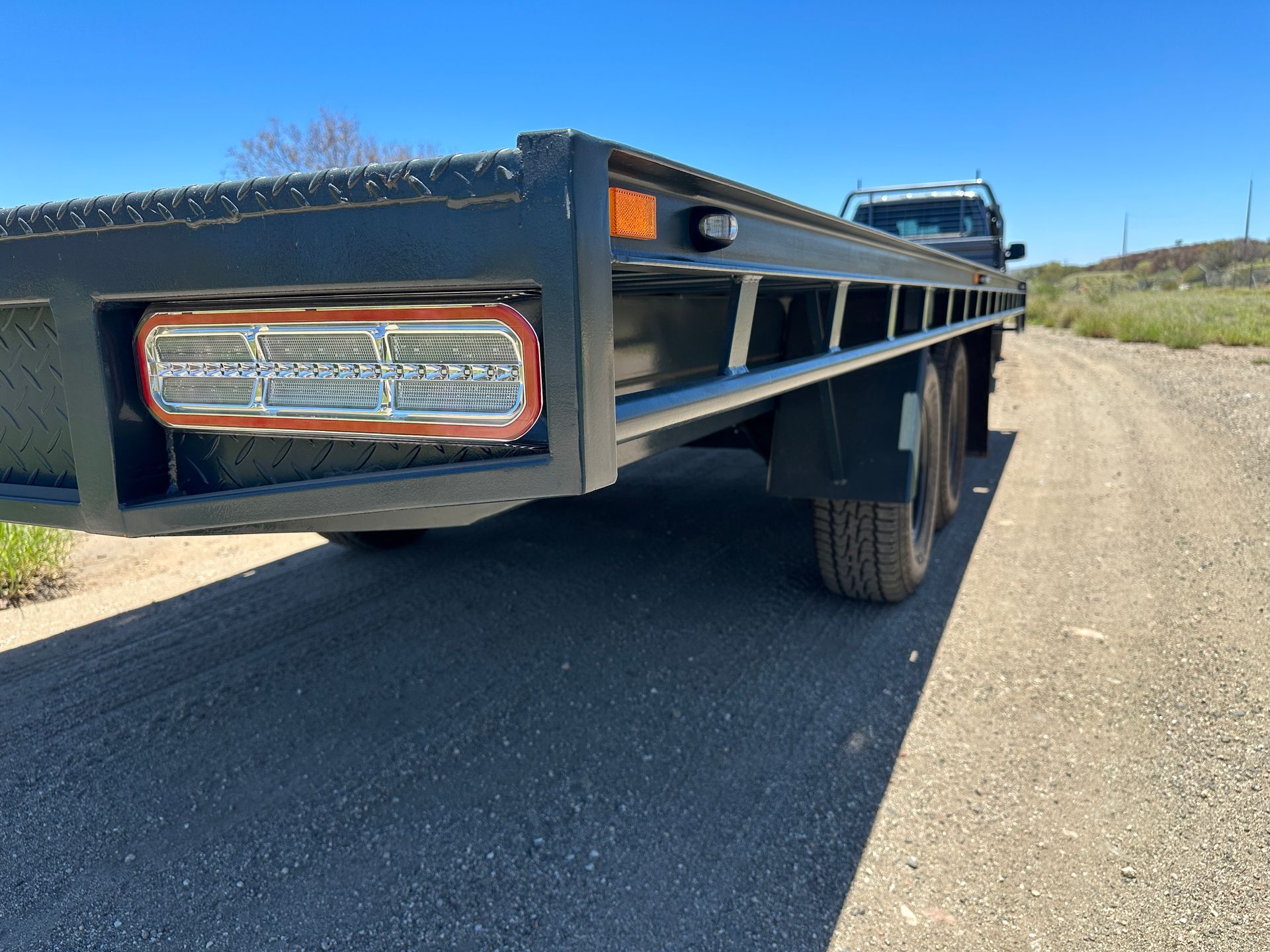 Black flatbed trailer parked on a rural dirt road, viewed from the rear corner