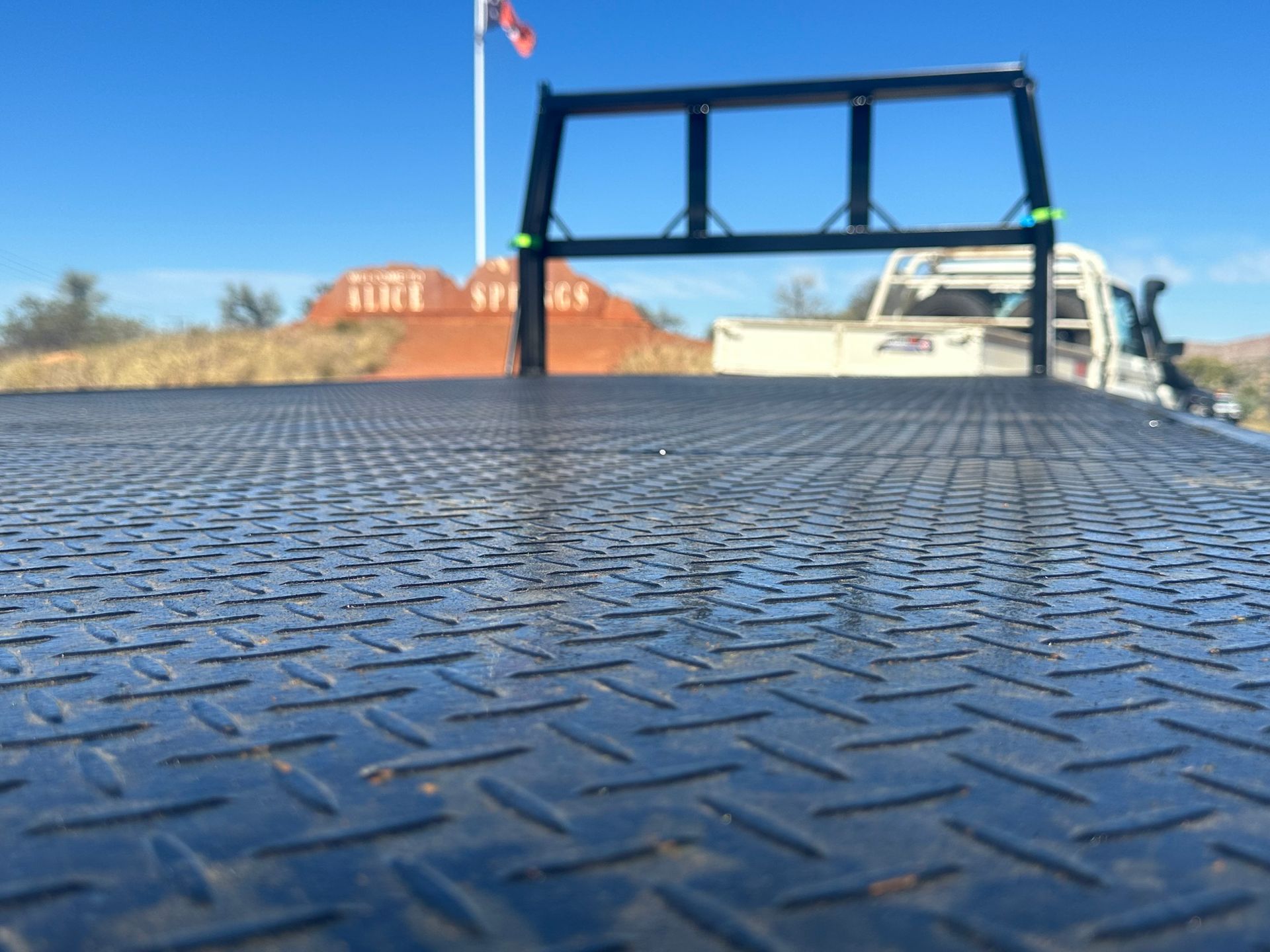 Textured metal truck bed with a blue frame, a white truck, and a red rock formation in the background.