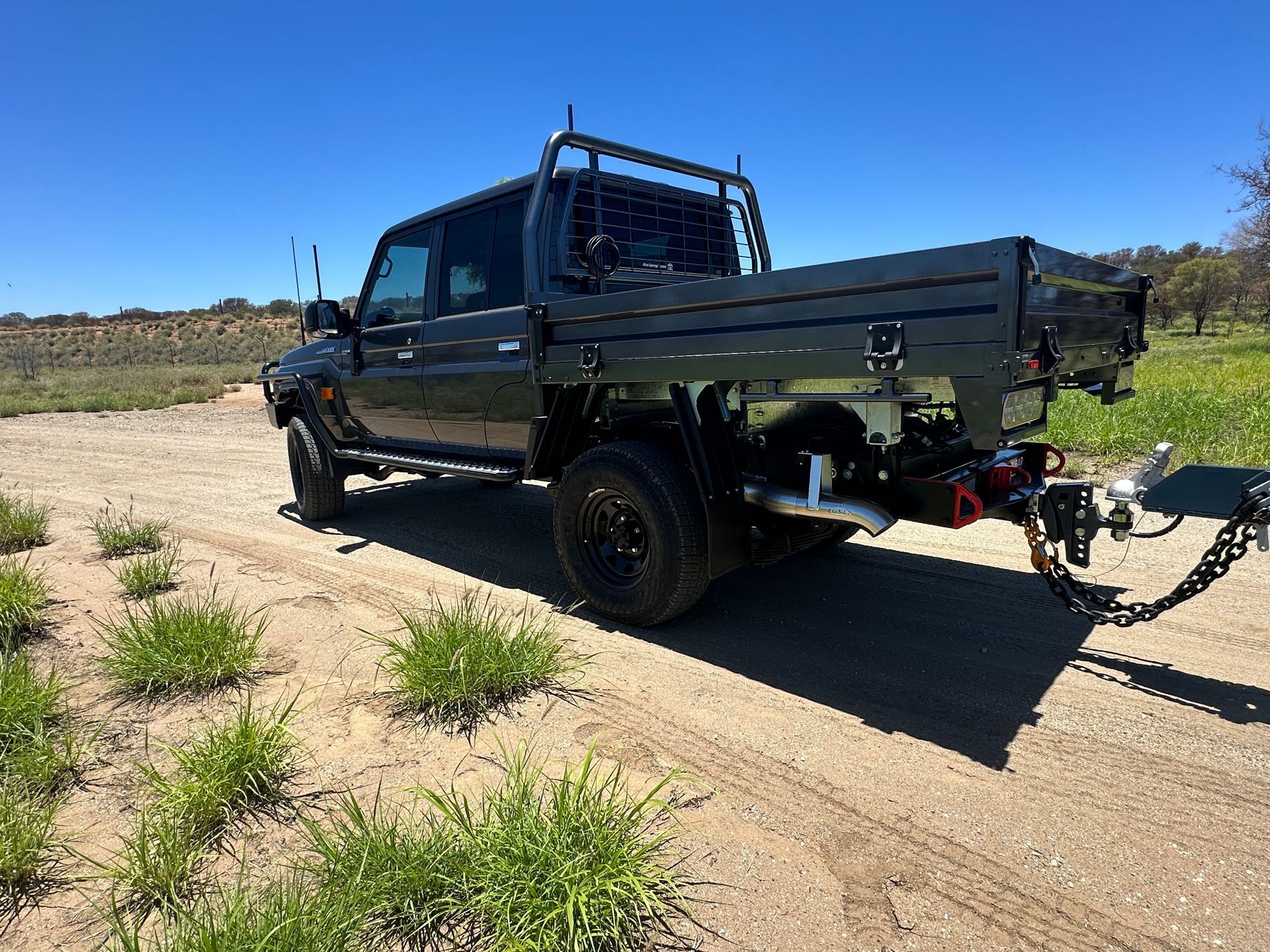 Black flatbed pickup truck with a tow hitch parked on a dirt road in a sunny rural area