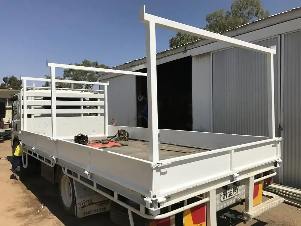 White utility trailer with metal frame parked outdoors beside a gray building.