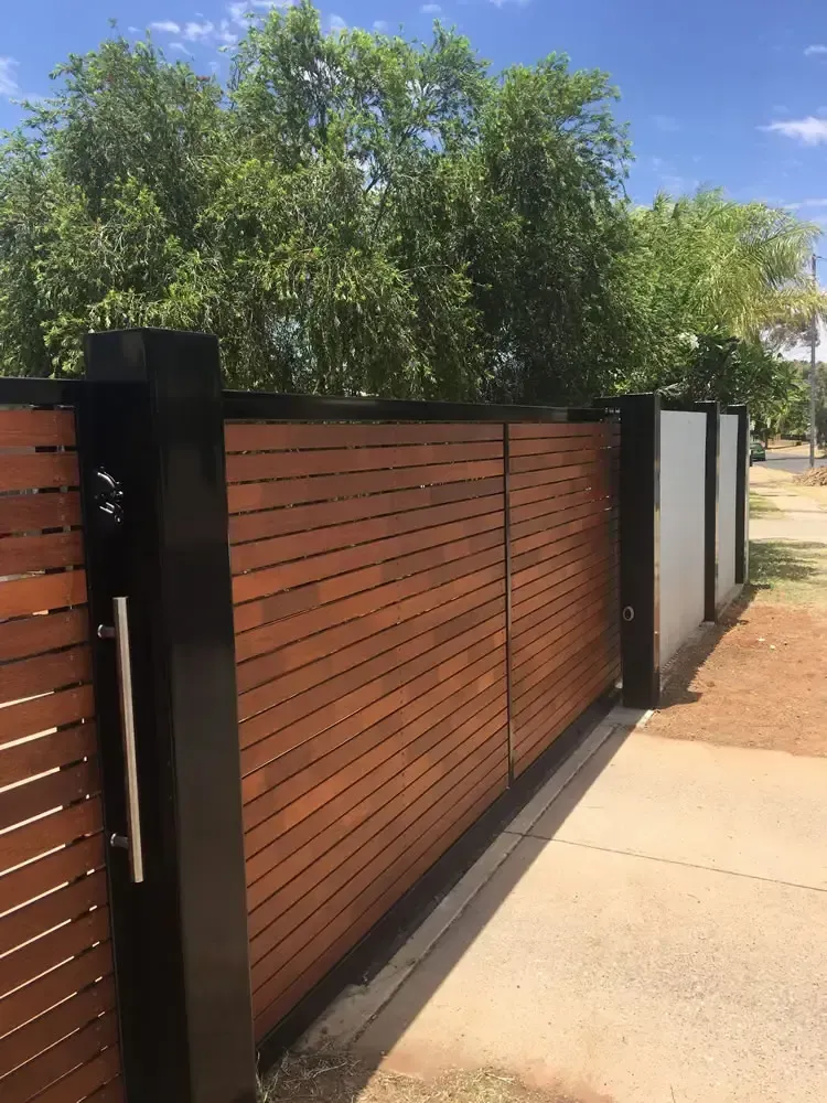 Modern wooden slat gate beside a sidewalk, with trees and blue sky in the background