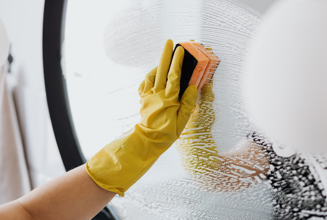 Hand in yellow glove cleans window with sponge.