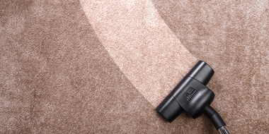 Vacuum cleaner cleaning a brown carpet, leaving a clean path.