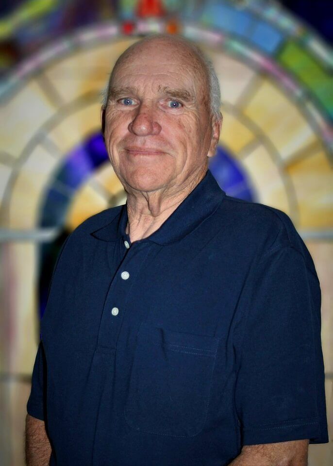 Portrait of a smiling man in a navy polo shirt against a colorful stained-glass background