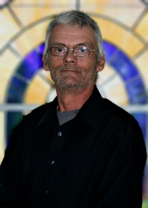 Man standing in a black shirt before a blurred stained-glass window backdrop
