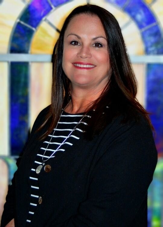 Smiling woman in black jacket standing before colorful stained-glass background