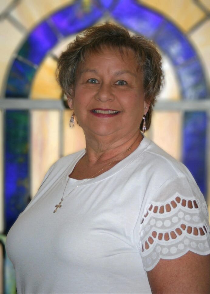 Woman smiling in a white shirt, standing before a stained-glass window.