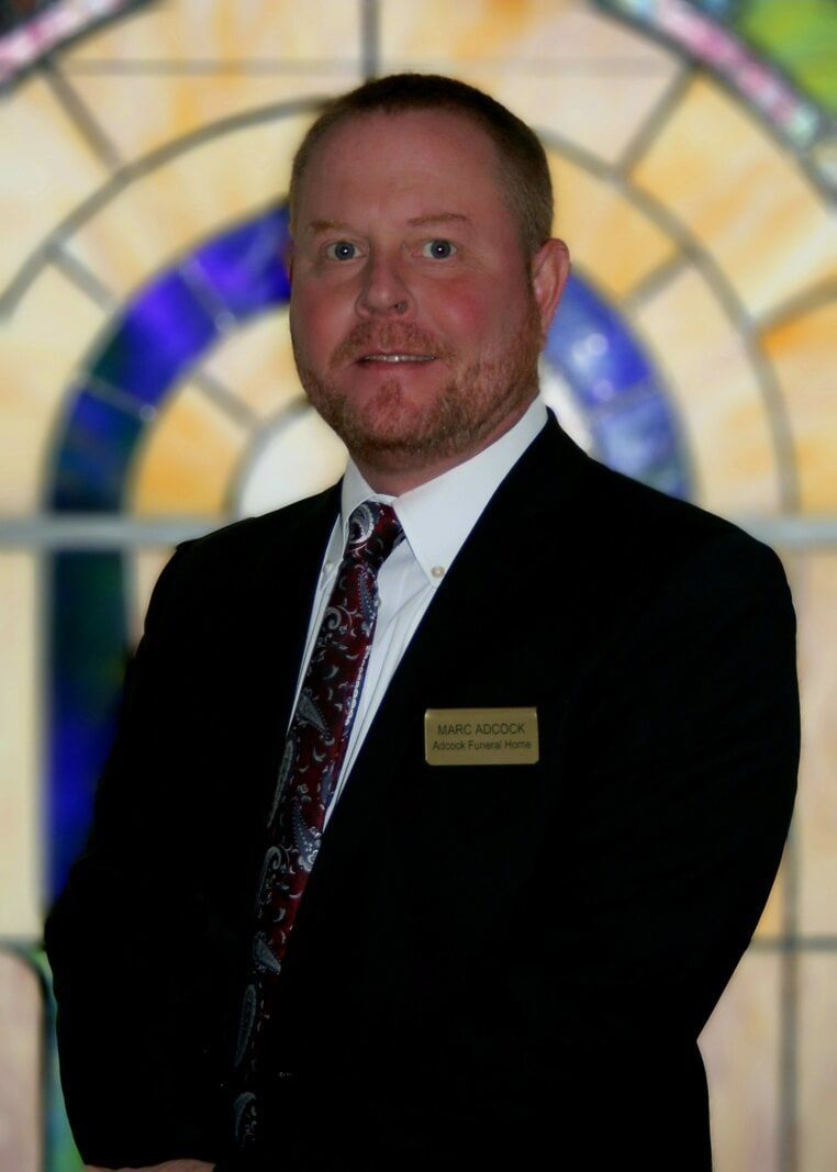 Man in a dark suit and tie standing before a stained-glass window